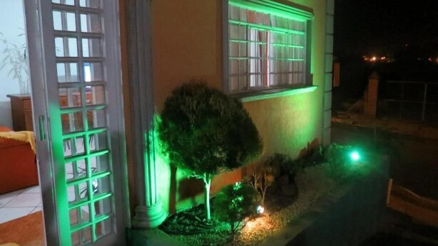 A building with large windows illuminated by green lights, a small tree, and a pathway leading to the entrance. - La Villa Hotel (Cordeirópolis)