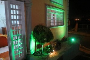 A building with large windows illuminated by green lights, a small tree, and a pathway leading to the entrance. - La Villa Hotel (Cordeirópolis)