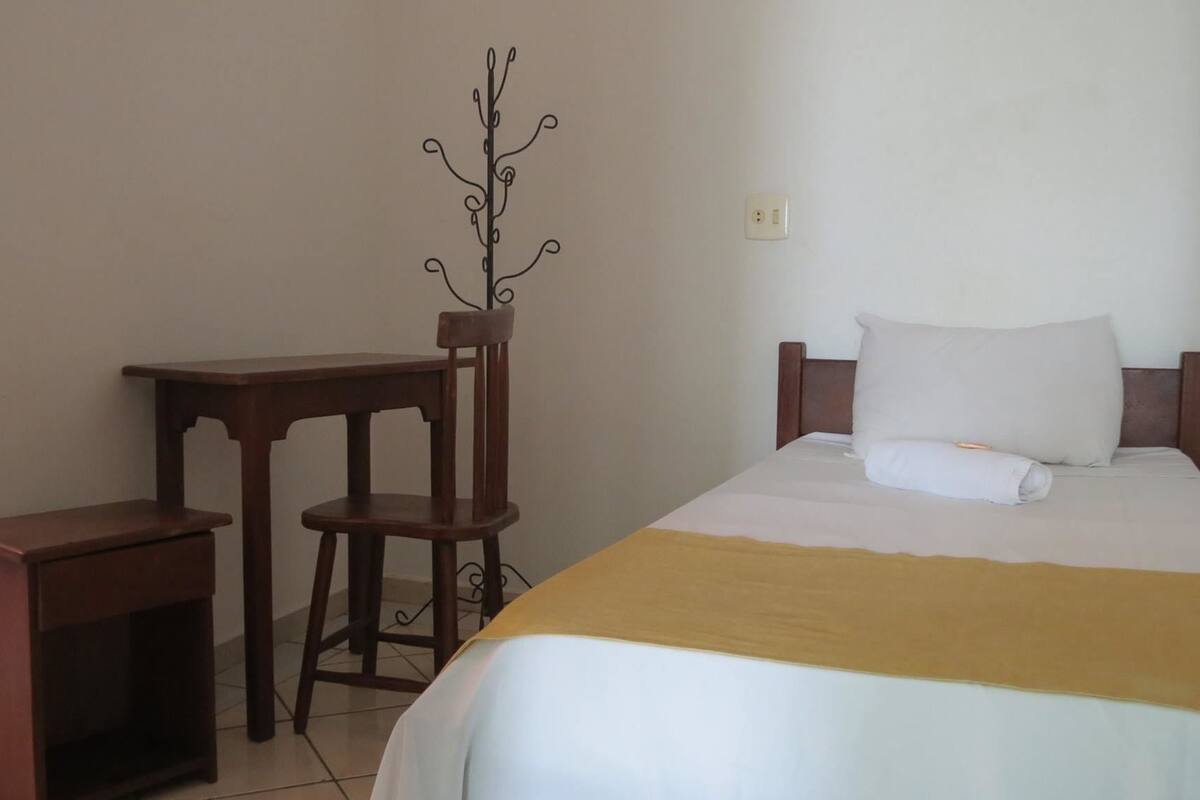 Une chambre à coucher comprenant un lit, une table de chevet, une chaise et un porte-manteau.