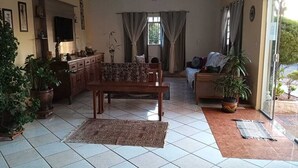 A living room with a sofa, a wooden table, and a television. There are potted plants and a rug on the floor. - La Villa Hotel (Cordeirópolis)
