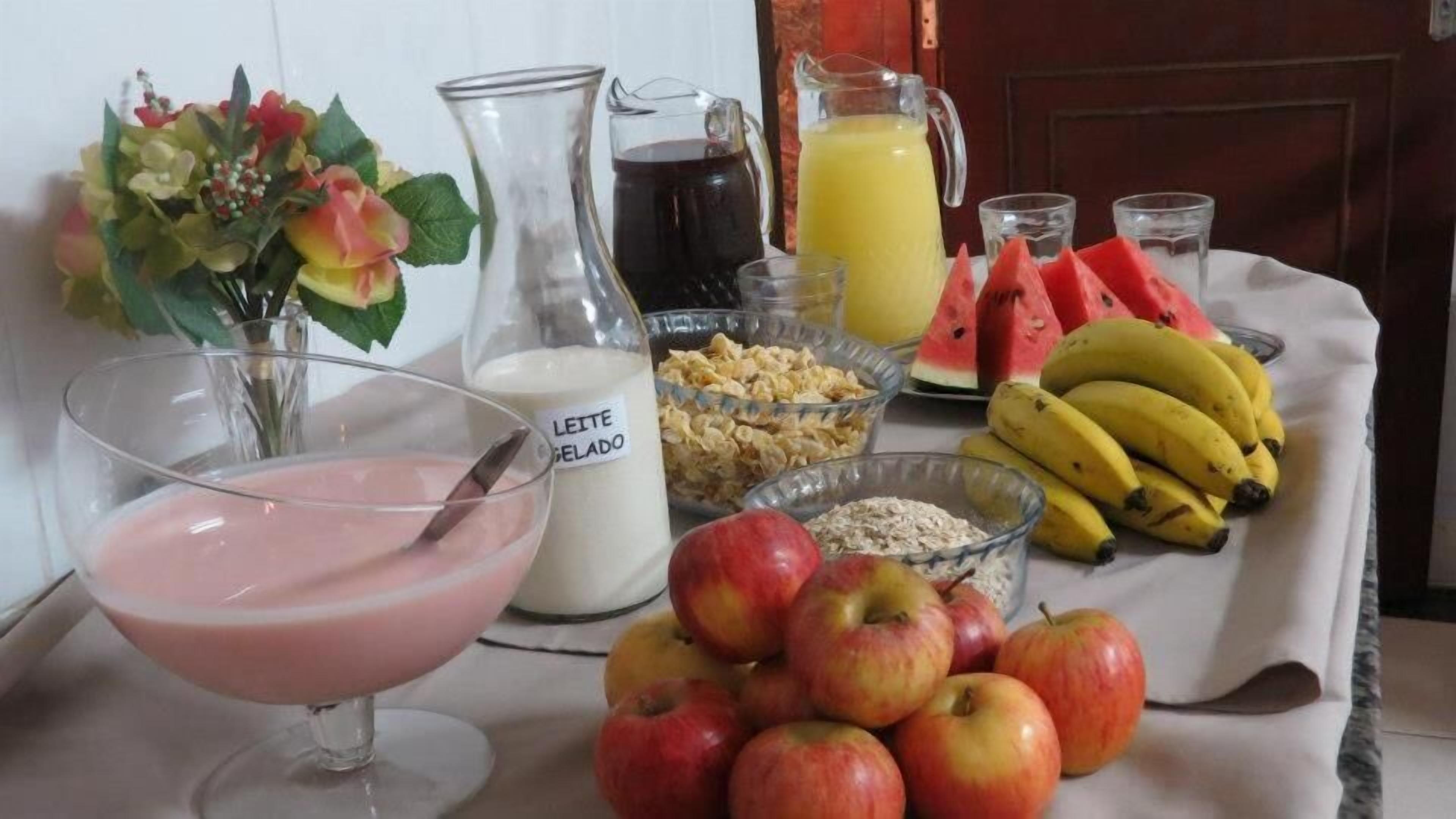 Una mesa de desayuno con una jarra de leche, un vaso de bebida rosada, frutas frescas y un tazón de cereal.
