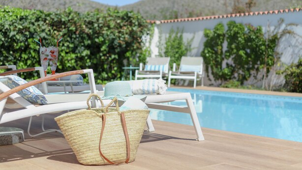 A poolside area with lounge chairs, a wicker basket, and a clear view of the pool and surrounding greenery.