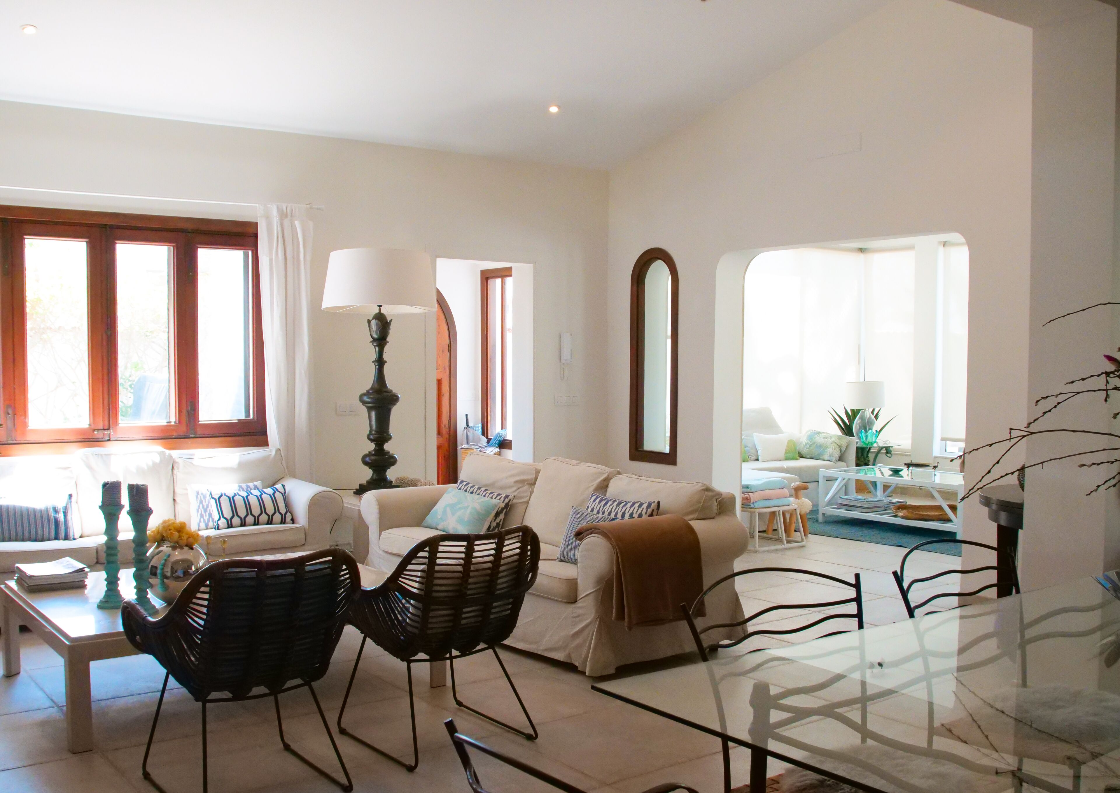 A living room with a sofa, two chairs, a glass coffee table, a lamp, and a view of the outside through large windows.