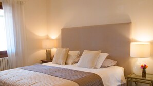 A neatly made bed with a quilted bedspread, two bedside tables with lamps, and a vase with flowers on one table.