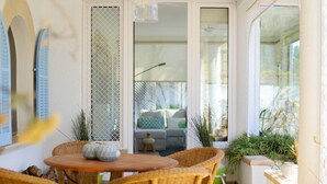 A sunlit patio with wicker furniture, a round table, and potted plants.