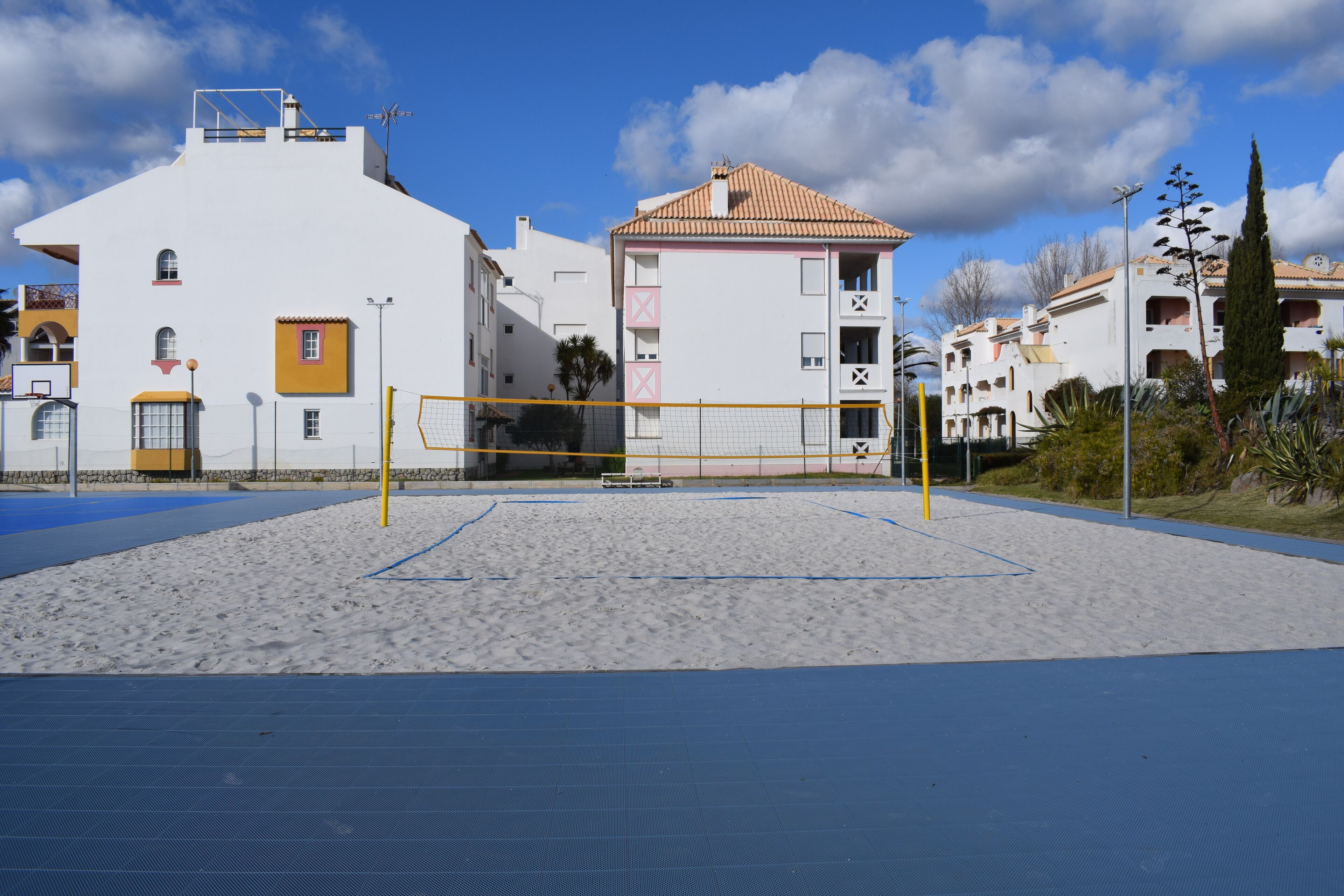 Ein Beachvolleyballfeld mit Netz, umgeben von Sand und blauer Bodenbelag.