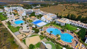 Ett flygbildsbild av ett semesterområde med flera pooler, tennisbanor och en mängd olika byggnader.