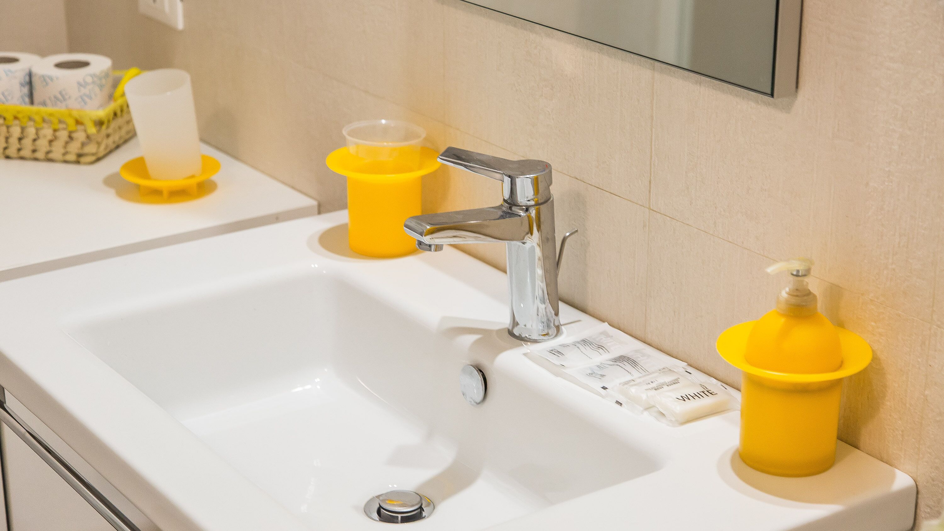 A bathroom sink with a chrome faucet, yellow soap dispensers, and a roll of toilet paper on the counter.