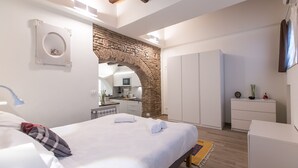 Een slaapkamer met een bed, een bureau, een kledingkast en een keuken, zichtbaar door een boog.