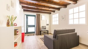 Een woonkamer met houten plafond, een televisie op een standaard, een bank en een boekenkast.