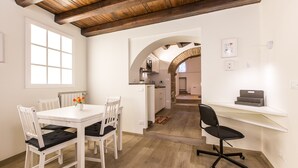 Een eethoek met een witte tafel en stoelen, een vaas met bloemen, en een keuken op de achtergrond.
