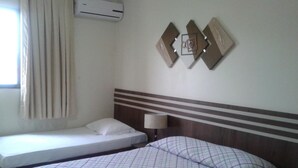 Ein Hotelzimmer mit zwei Betten, einem fensterbelaubten Fenster, einer Klimaanlage und einer Wandlampe.