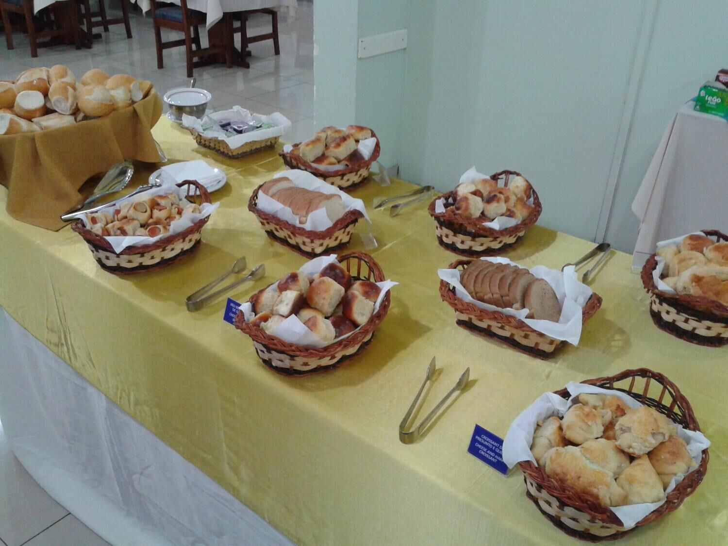 A buffet table with various baked goods in baskets, utensils, and a tablecloth.