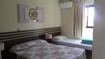 Quarto de hotel com duas camas, ar condicionado fixado na parede, janela com cortinas e um objeto decorativo na parede.