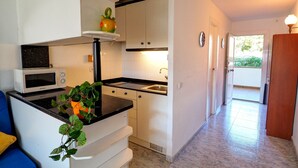 A compact kitchen with white cabinets, a microwave, and a sink. There is a plant on the counter and a blue chair in the corner. - The Moon Studio by Hello Homes Sitges (Sitges)