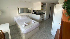 A hotel room with a bed, a small desk, a mirror, a kitchenette, and a refrigerator. - The Moon Studio by Hello Homes Sitges (Sitges)