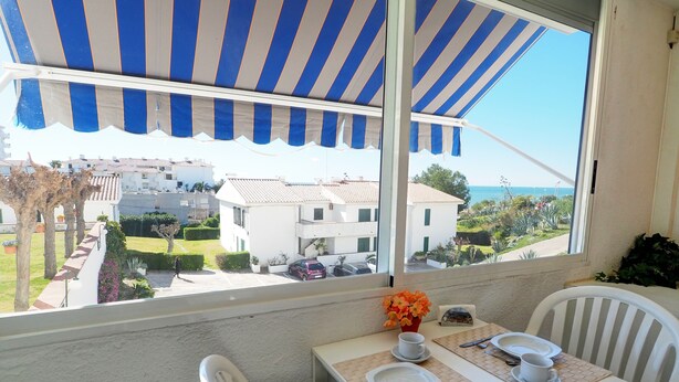 A balcony with a table set for two, a view of the sea, and a blue and white striped awning. - The Moon Studio by Hello Homes Sitges (Sitges)