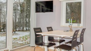 A dining area with a table and chairs, a TV mounted on the wall, and a window with a view of trees and snow. - 2 bedroom awesome home in Kvidinge (Kvidinge)