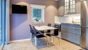 A modern kitchen with a dining area, featuring a flat-screen TV, a window with a view of trees, and stainless steel appliances. - 2 bedroom awesome home in Kvidinge (Kvidinge)