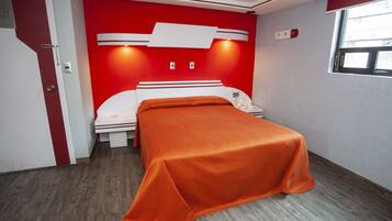 A hotel room with a red accent wall, a white bed, and a wooden floor.