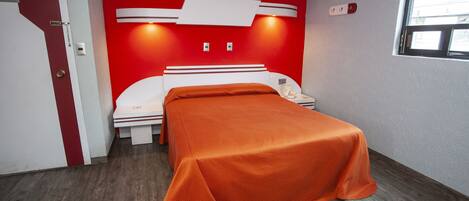 Una habitación de hotel con una pared de acento roja, una cama blanca y suelo de madera.