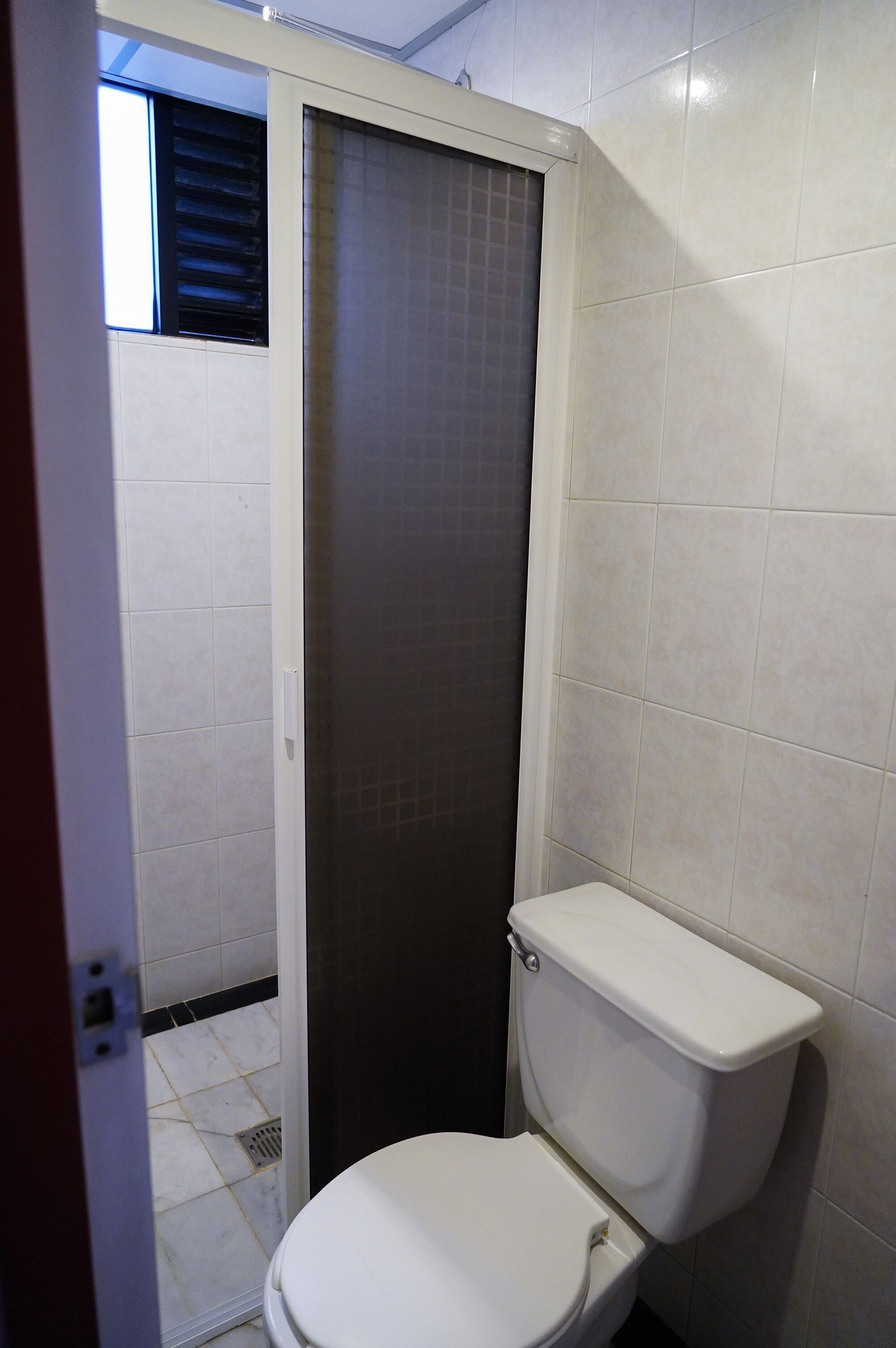 Un baño con inodoro, zona de ducha y ventana con persianas.