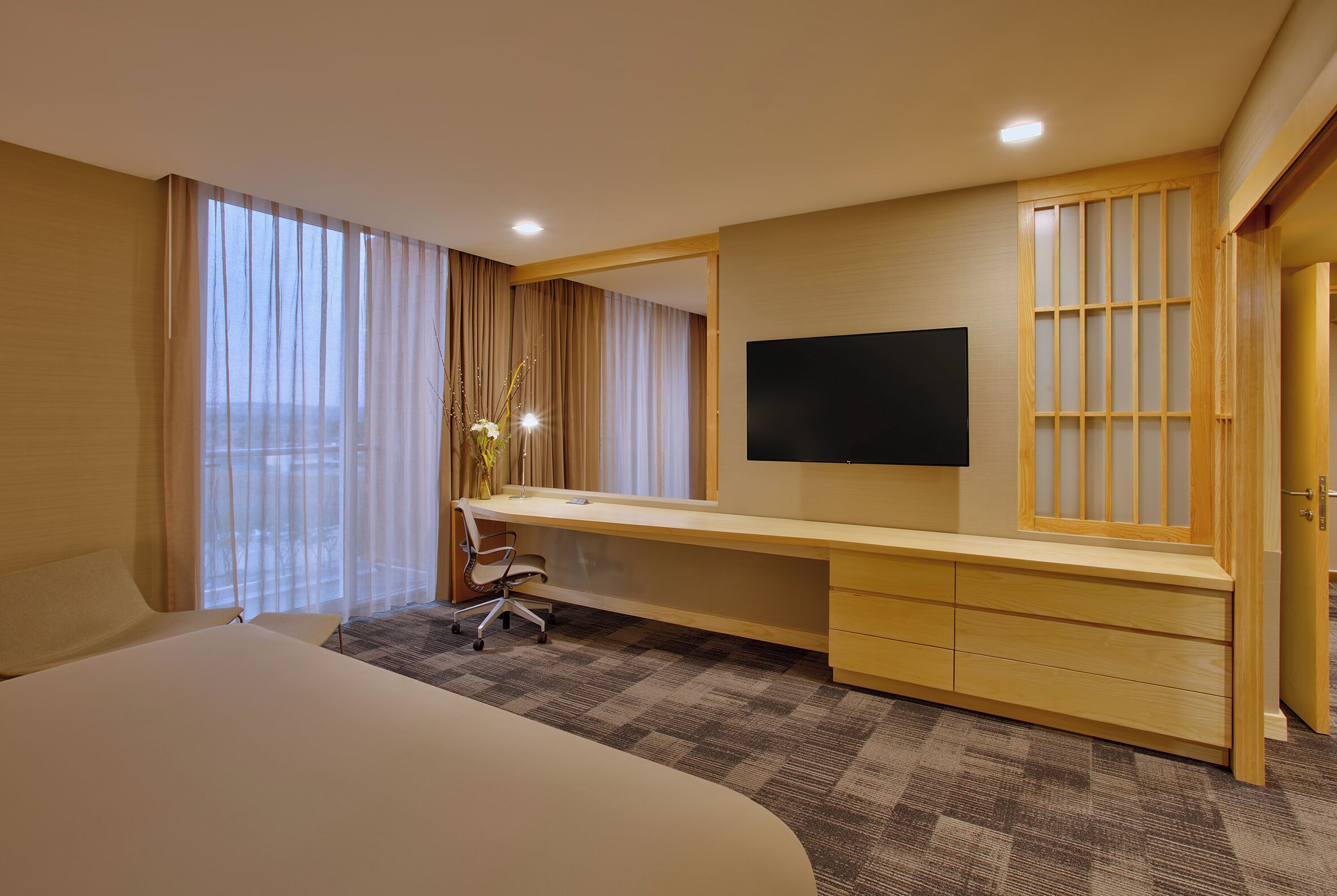 A hotel room with a large bed, a desk with a chair, a TV, and a window with curtains.