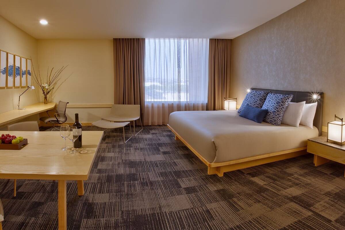 Une chambre d’hôtel comprenant un lit, des tables de chevet, un bureau avec une chaise, une télévision et une fenêtre avec des rideaux.