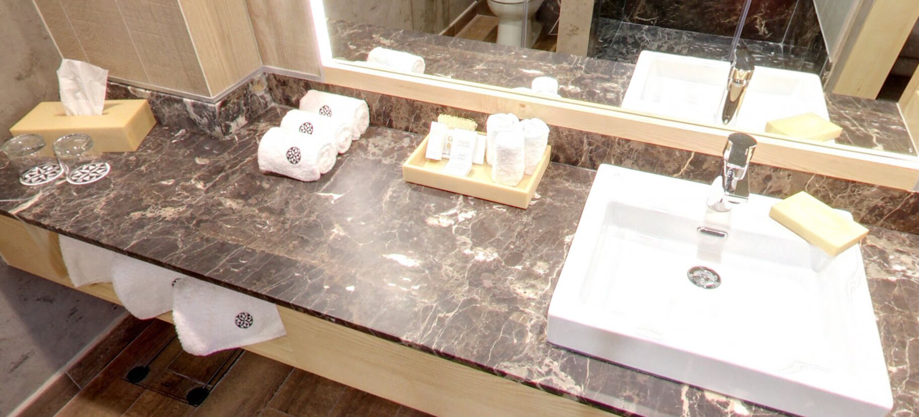 A bathroom with a marble countertop, two sinks, a mirror, and toiletries.