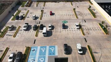 Vista aérea de um estacionamento com várias fileiras de vagas, algumas delas reservadas para deficientes, e alguns carros estacionados.