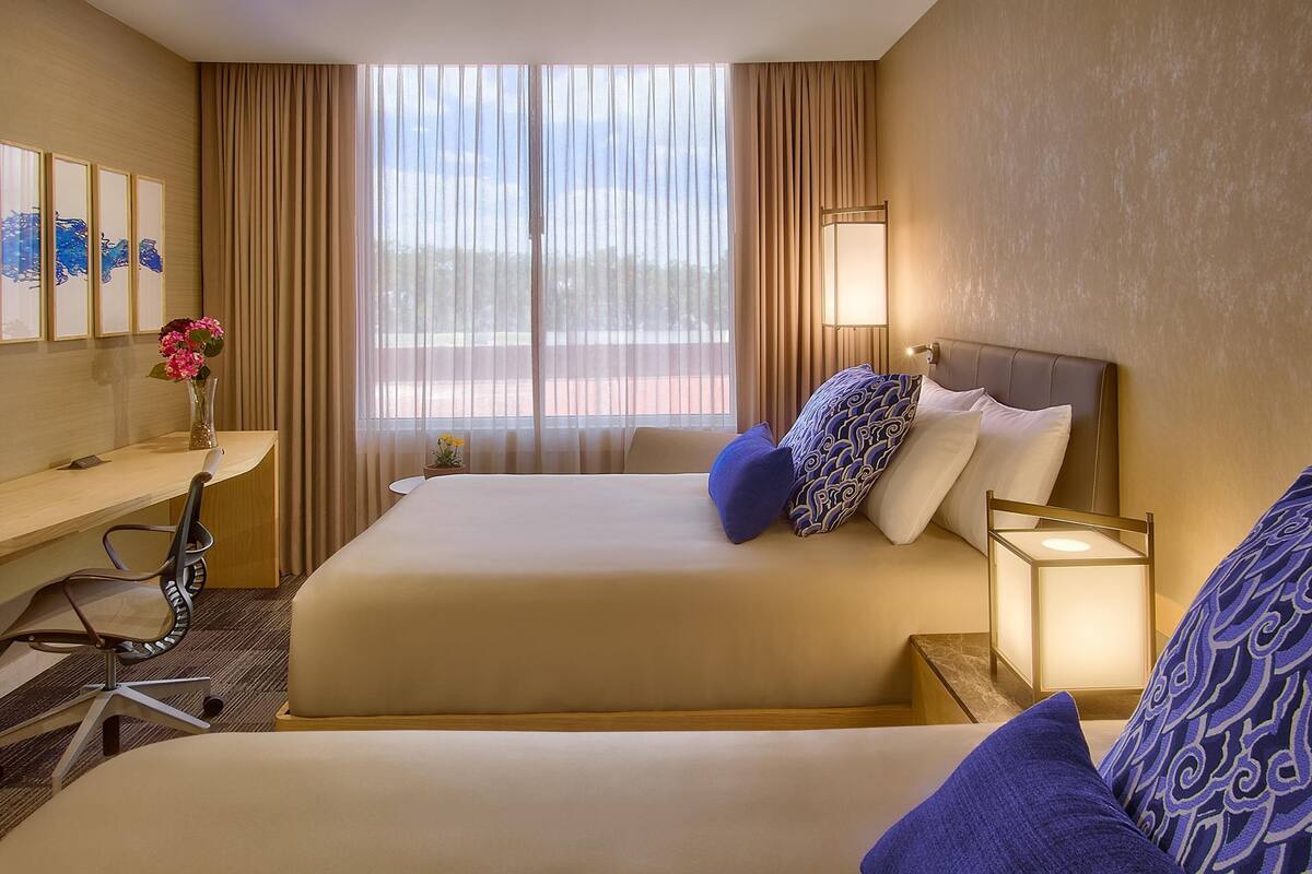 Une chambre d’hôtel équipée d’un lit, d’un bureau, d’une chaise, d’une lampe et d’une œuvre d’art au mur.