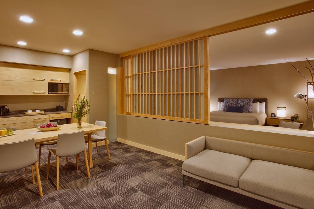Une chambre d’hôtel moderne dotée d’un coin repas, d’un canapé et d’une grande fenêtre offrant une vue dégagée.