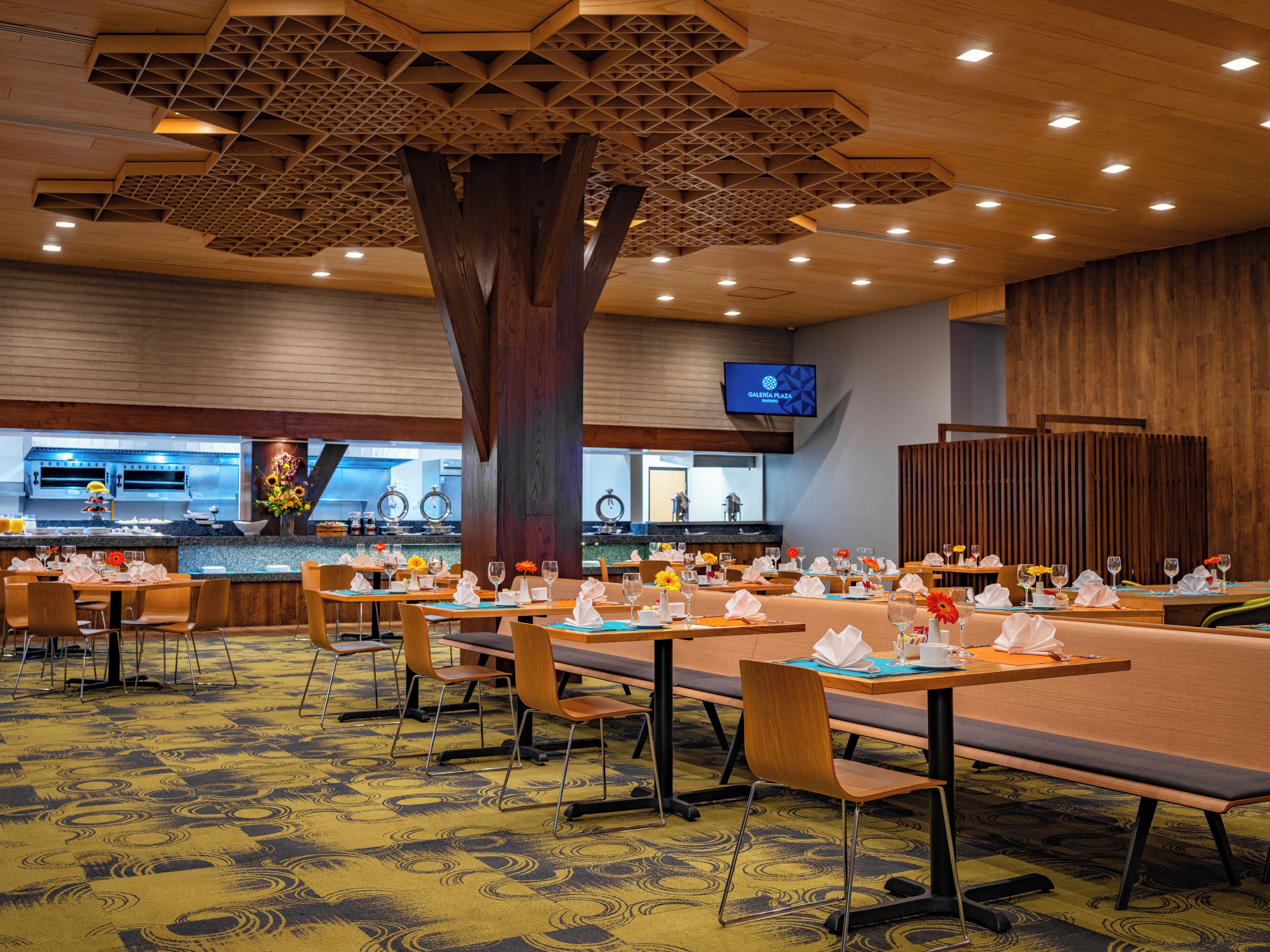 Un restaurante con varias mesas y sillas, una gran estructura parecida a un árbol en el centro, y una cocina al fondo.