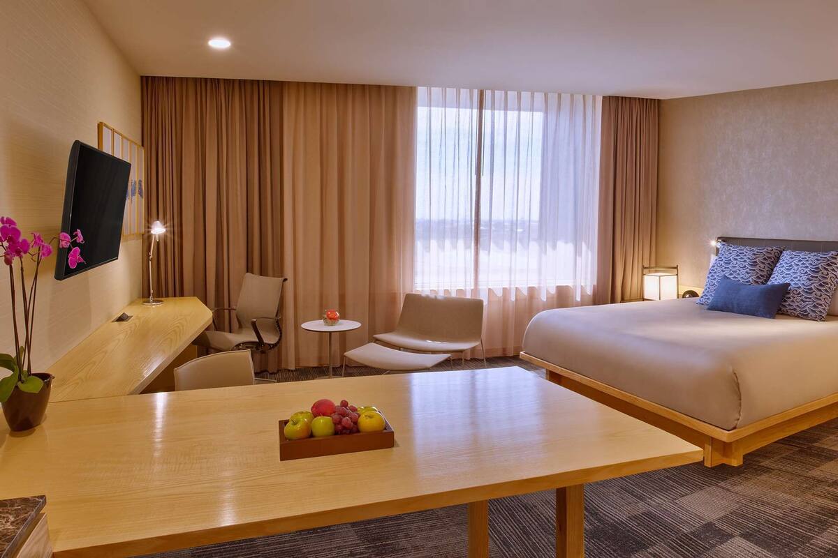 Une chambre d’hôtel avec un lit, un bureau agrémenté d’un panier de fruits, une chaise, une petite table et un téléviseur fixé au mur.
