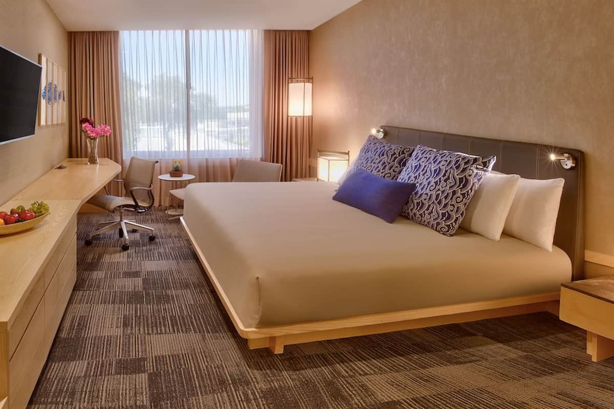 Une chambre d’hôtel avec un lit, un bureau, une chaise, une télévision et une petite table agrémentée de fleurs.