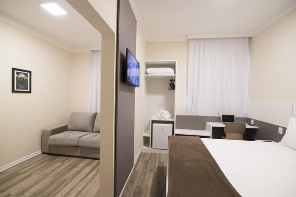 Una habitación de hotel con cama, escritorio, silla, televisor y una pequeña cocina.