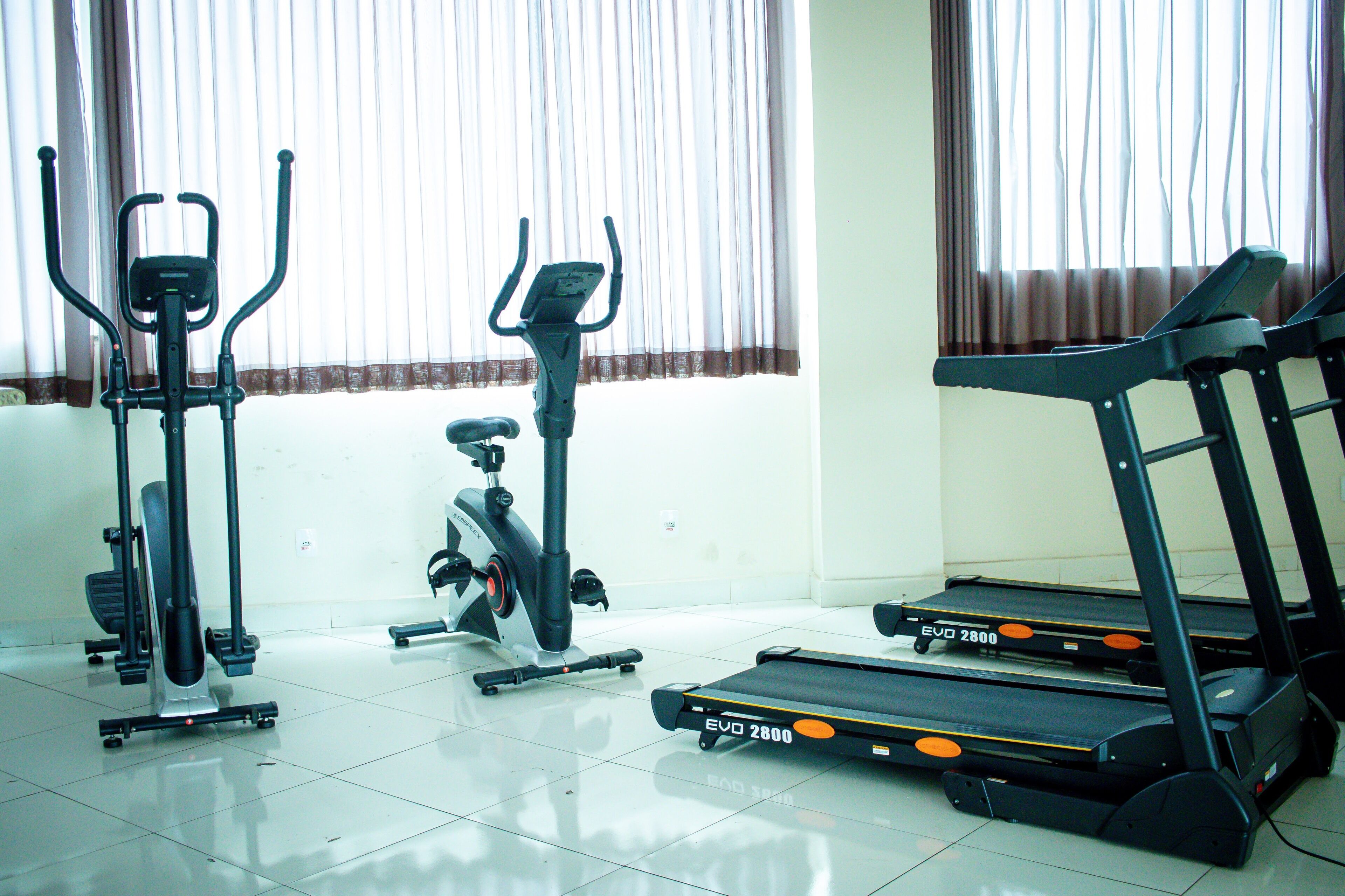 Quarto com equipamentos de ginástica, incluindo bicicleta ergométrica, elíptico e esteiras.