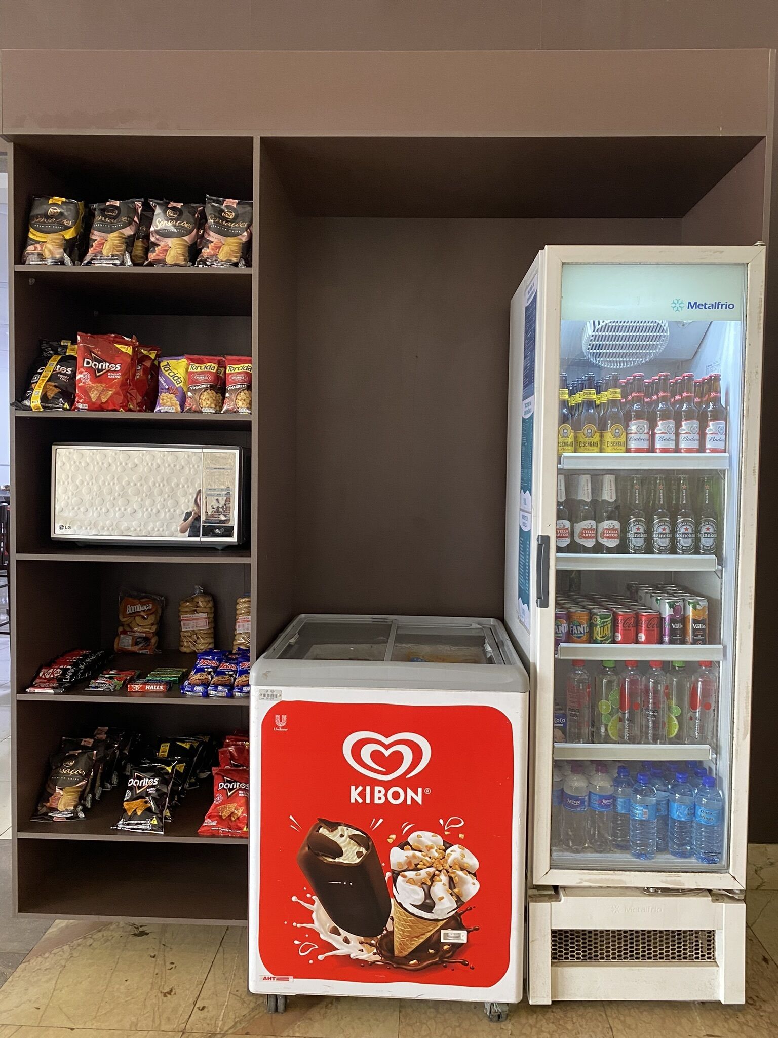Ein Getränkeautomat mit Kibon-Eisbechern, umgeben von Regalen voller Snacks und Getränke.
