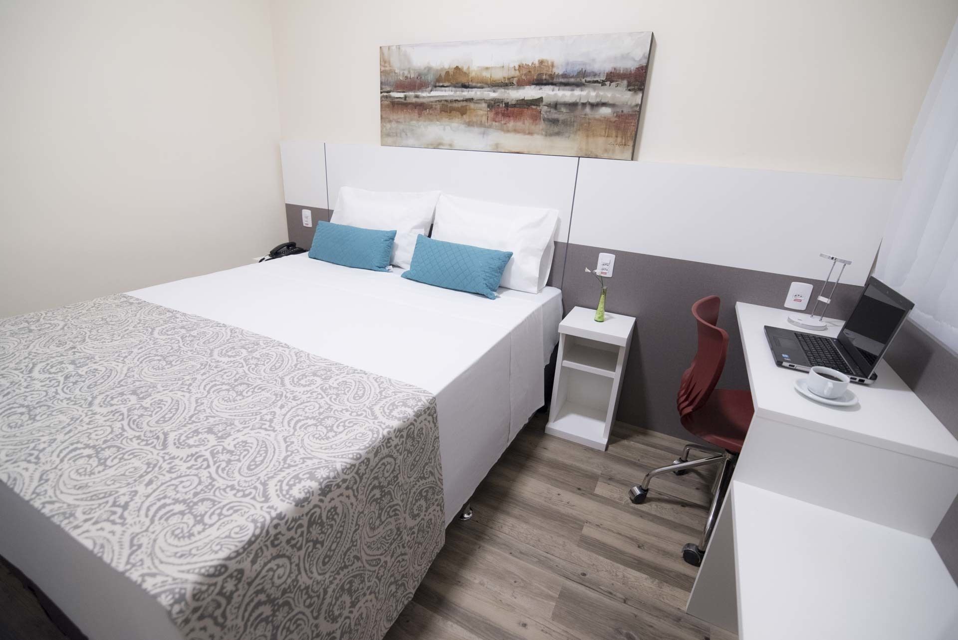 Ein Hotelzimmer mit einem Bett, einem Schreibtisch mit einem Laptop und einem Bild an der Wand.