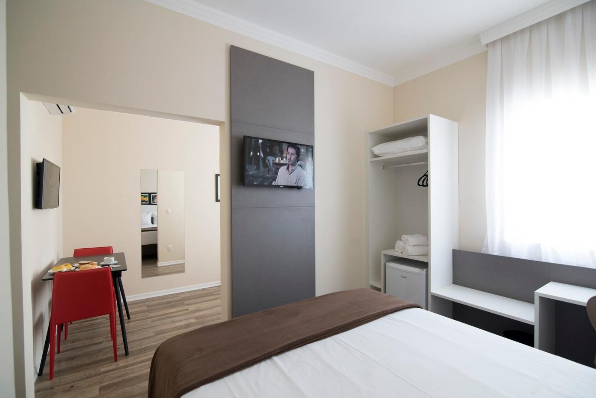 Una habitación de hotel con cama, escritorio, silla, televisor y armario.