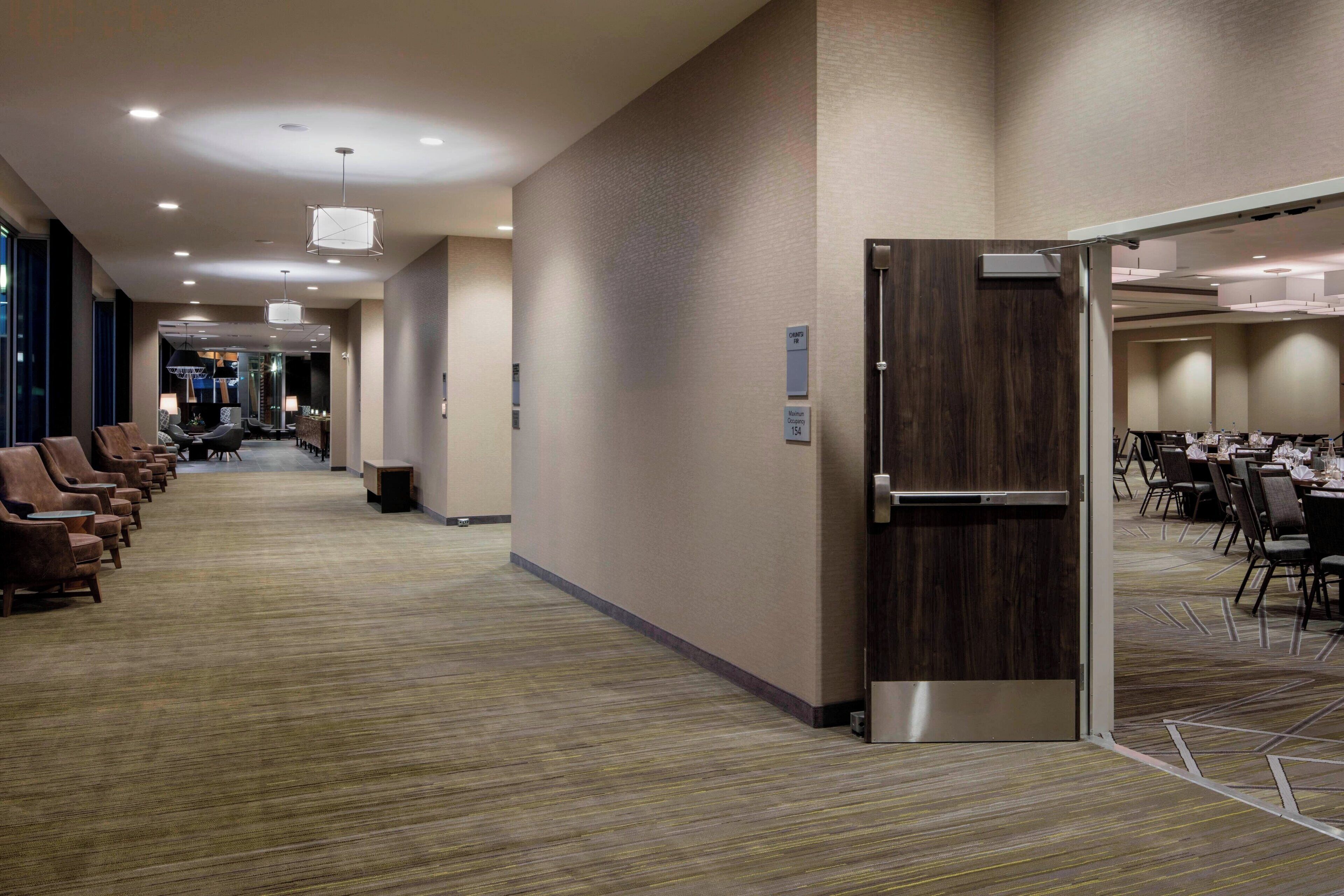 A hotel corridor with seating areas, a conference room, and a reception desk.