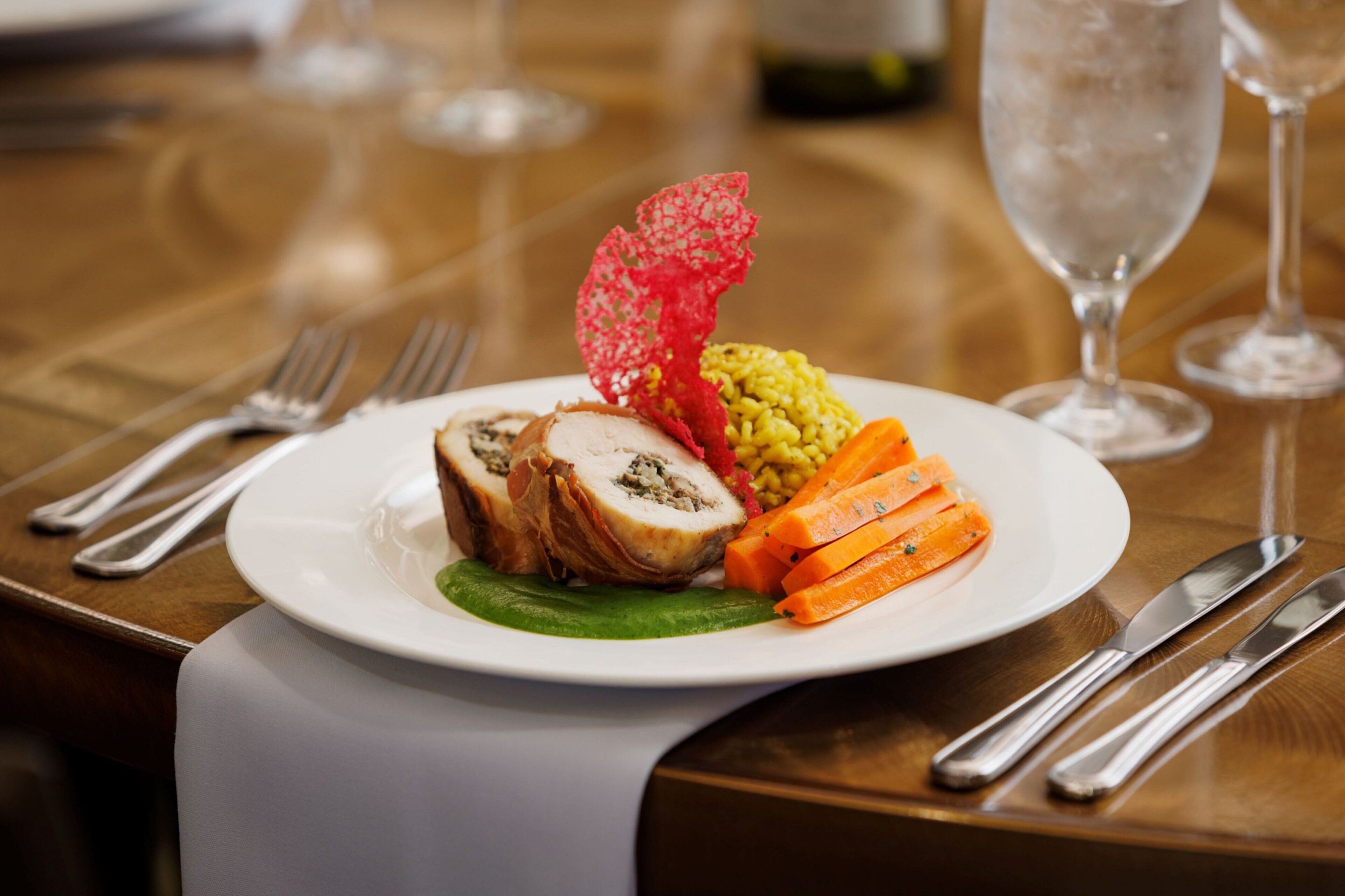 A plate of food with a rolled meat dish, yellow rice, and sliced carrots on a white plate.