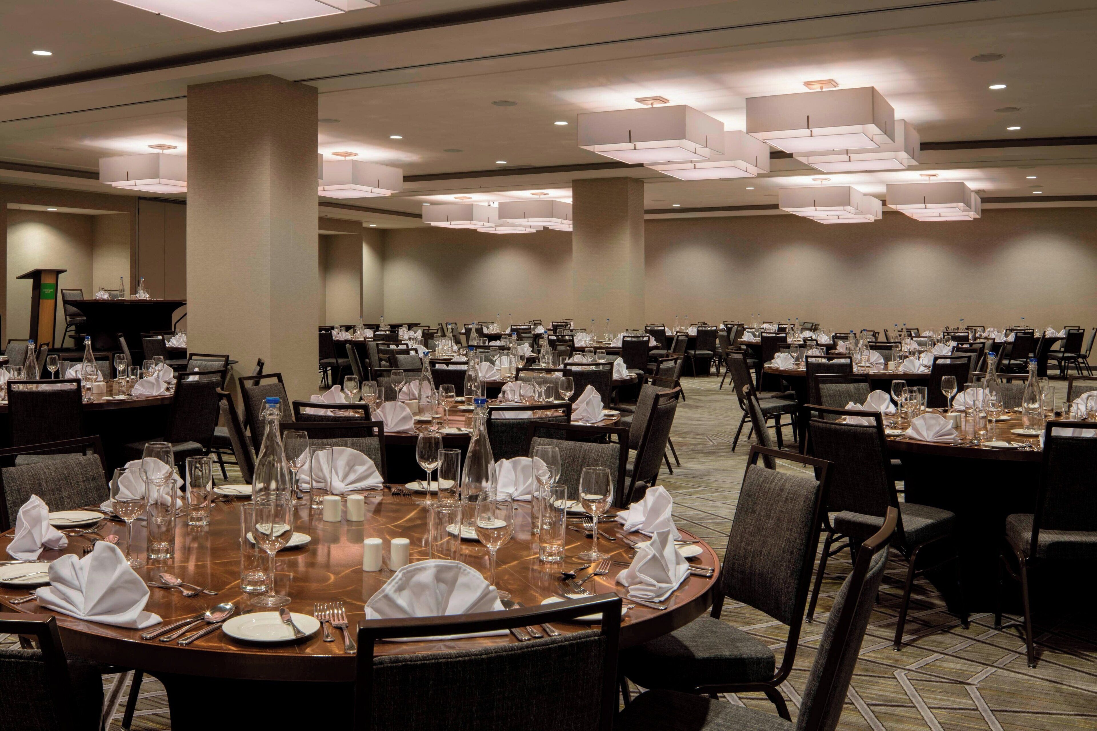 A large banquet hall with multiple round tables set for dining, each with white tablecloths, plates, and cutlery.