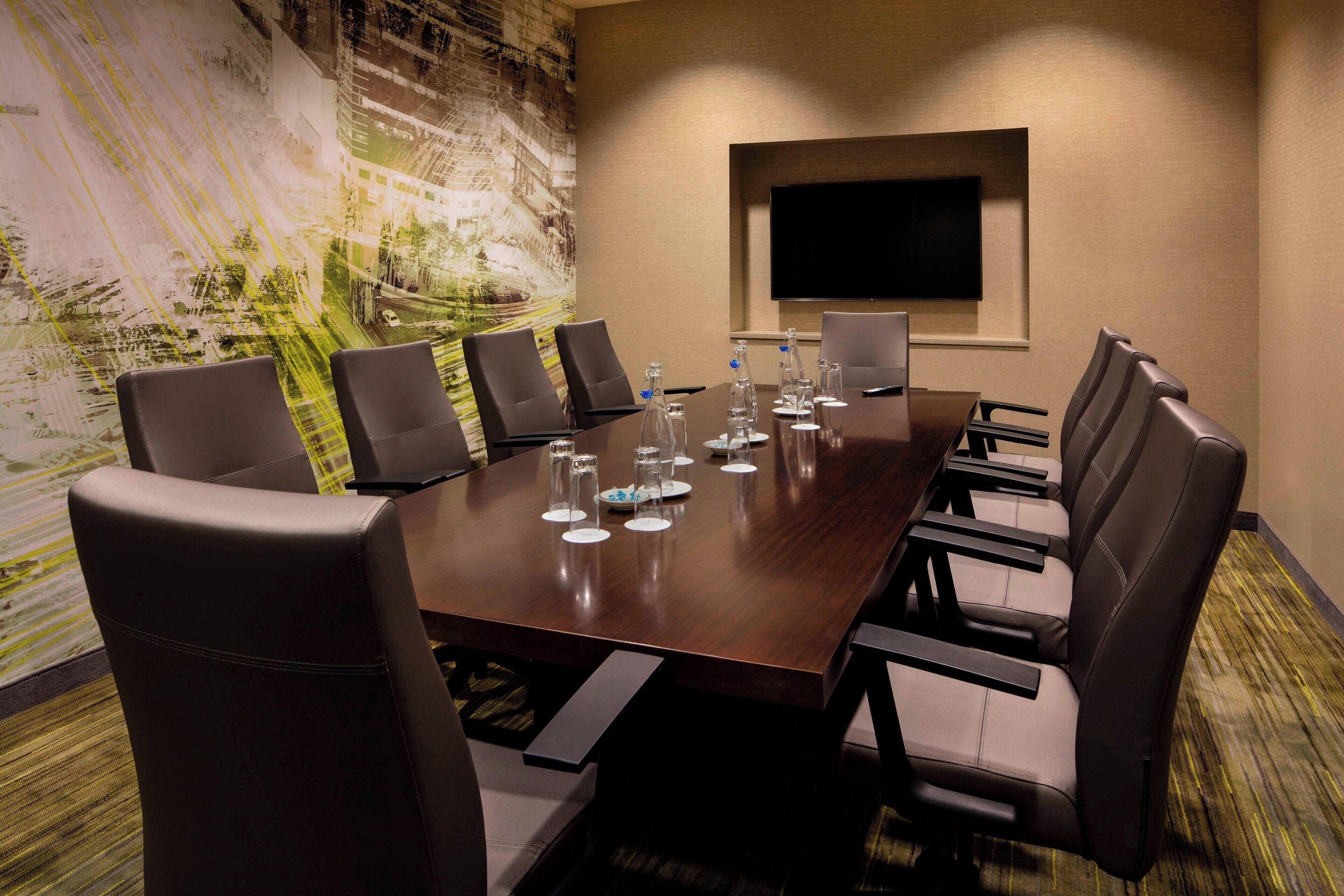 A conference room with a long table, six chairs, and a flat-screen TV on the wall.