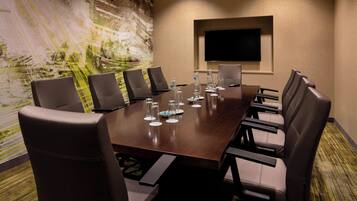 A conference room with a long table, six chairs, and a flat-screen TV on the wall.