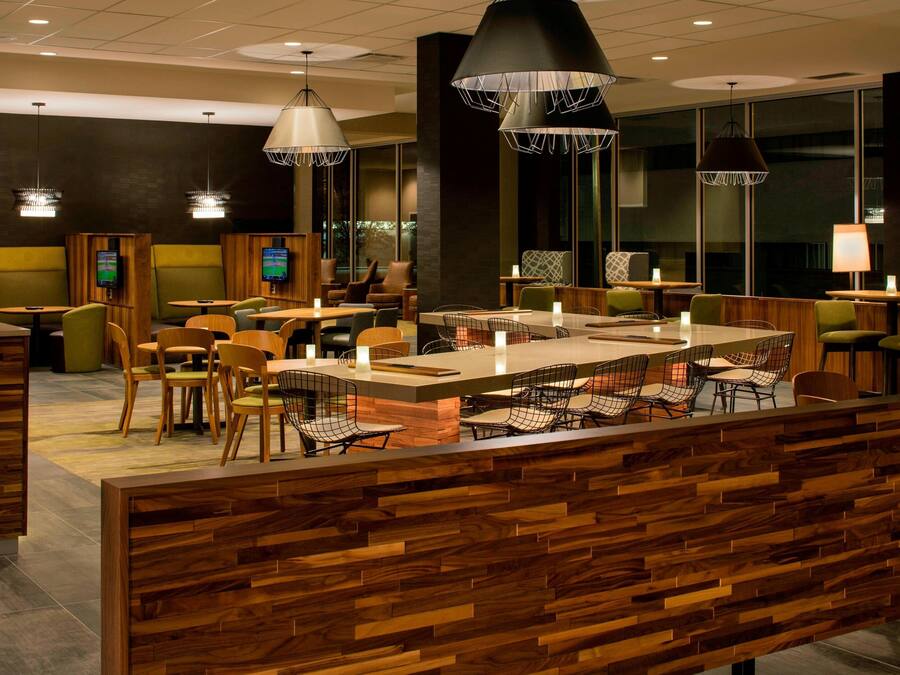 A modern restaurant with wooden accents, multiple seating areas, and pendant lighting.