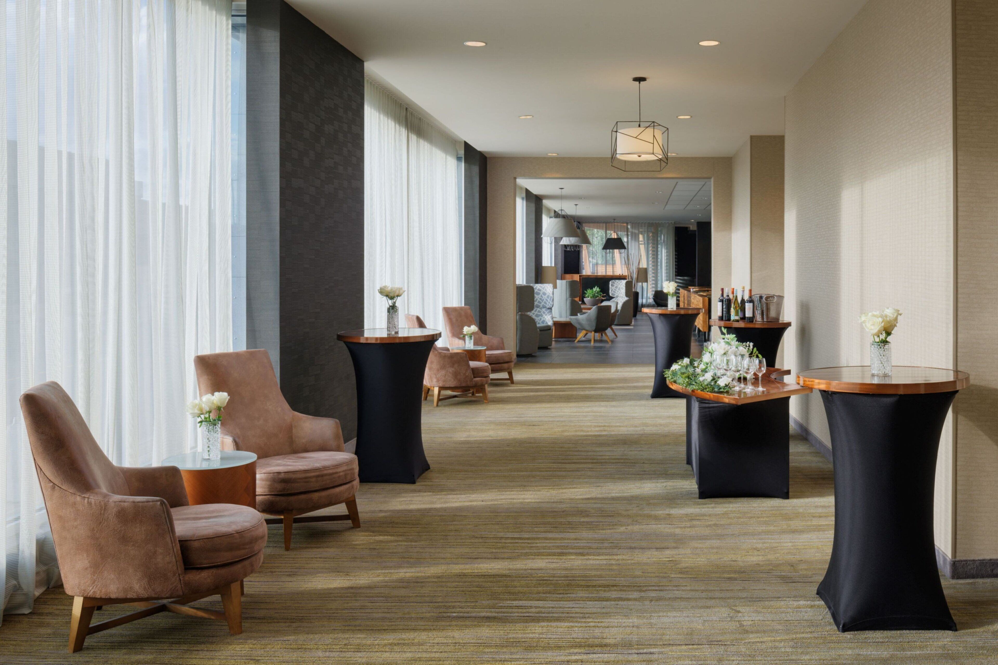 Un vestíbulo de hotel con sillones de cuero, mesas redondas y suelo alfombrado.