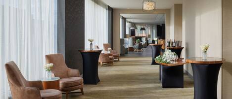 Un vestíbulo de hotel con sillones de cuero, mesas redondas y suelo alfombrado.