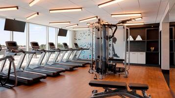 Et fitnessrum med løbebånd, bænk og styrkemaskiner.