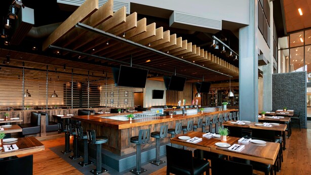 Un restaurante moderno con una barra larga, taburetes y mesas de madera.
